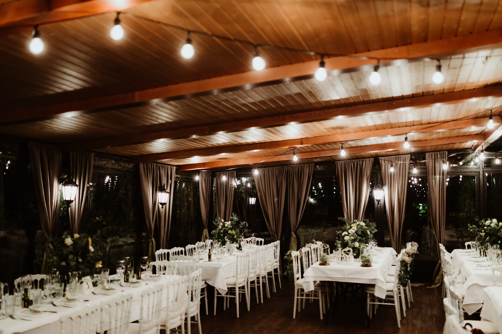 Restoran pod string lightovima sa belim stolovima i zelenilom