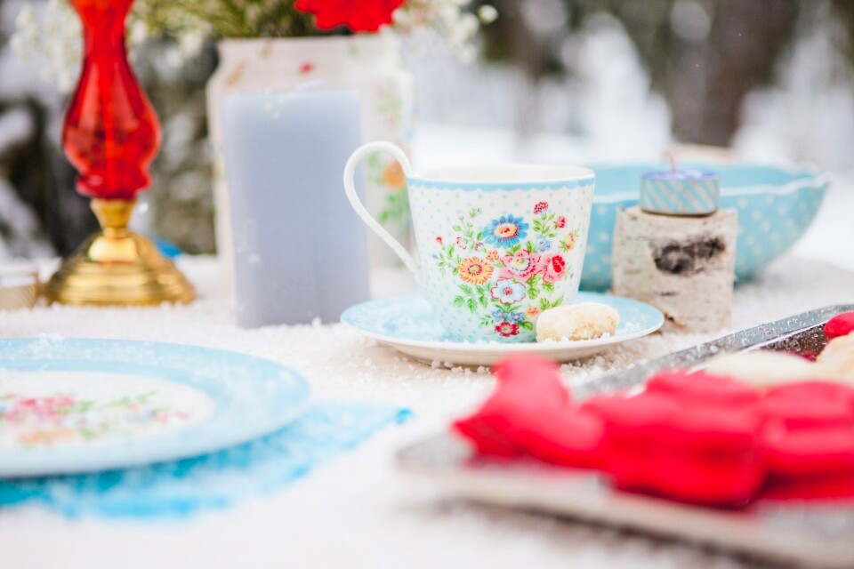 Porcelanske šoljice sa cvetnim motivom, crveni makaronsi i sveća na snežnom stolu